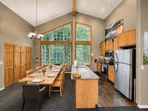 Une cuisine spacieuse avec un grand îlot central, des meubles en bois et une vue à travers une fenêtre à vitres teintées de vert.
