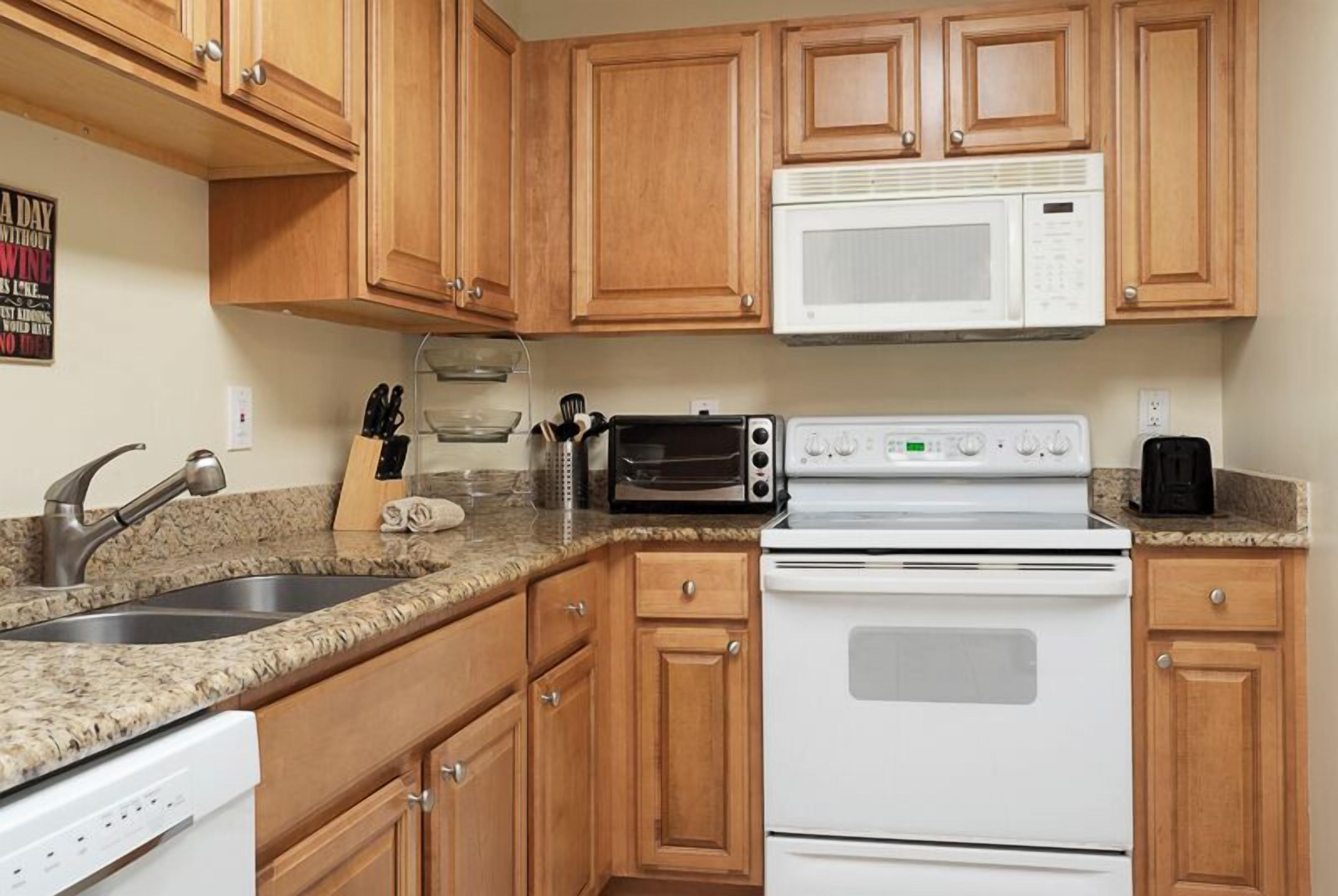 A kitchen with wooden cabinets, a white microwave, a toaster oven, a stove, and a dishwasher.