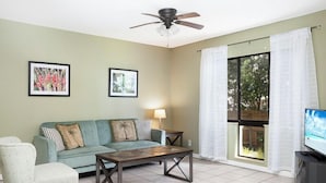 A living room with a sofa, armchair, coffee table, ceiling fan, and a TV. - Condos at Wander Residences in Tierra Verde (Tierra Verde)