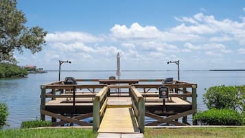 Un muelle de madera con una mesa de picnic y bancos, con vista a un cuerpo de agua.