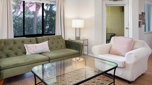 A living room with a green sofa, a white armchair, a glass coffee table, and a lamp. - Condos at Wander Residences in Tierra Verde (Tierra Verde)