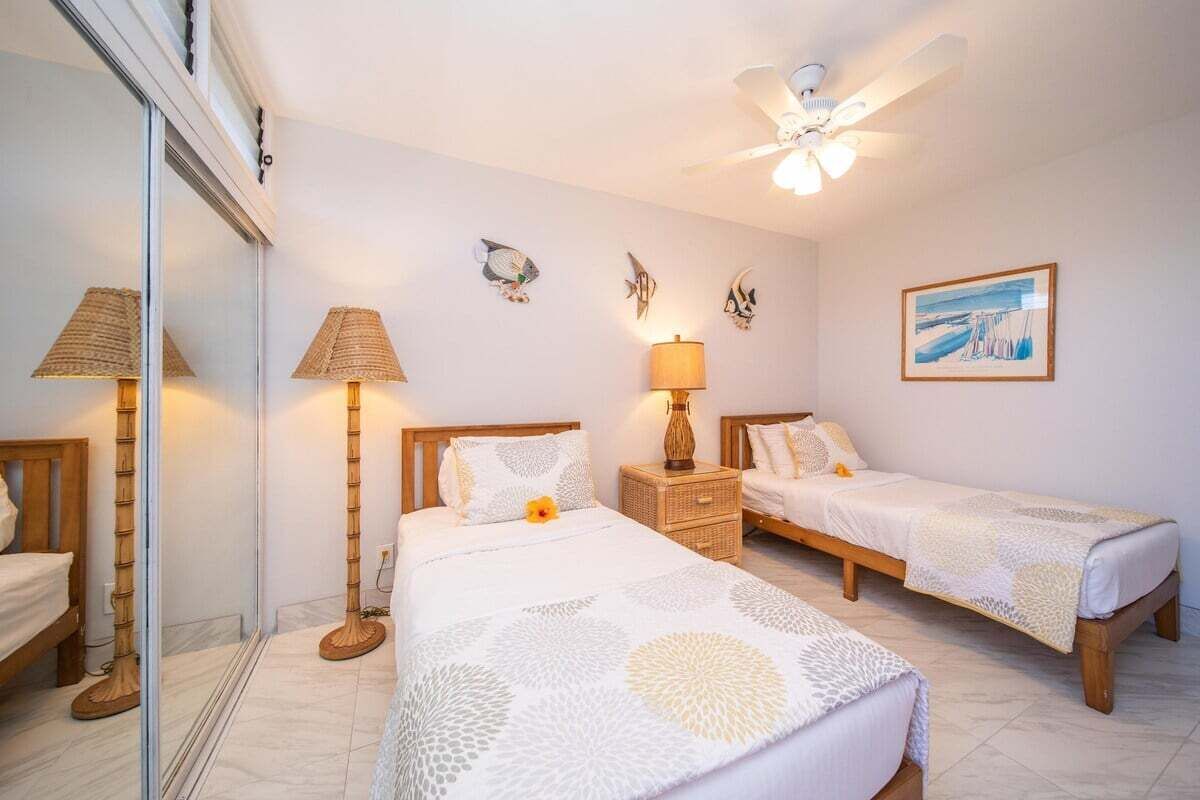 A hotel room with two single beds, a ceiling fan, a bedside table with a lamp, and a wall-mounted fish decoration.