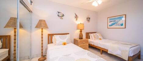 A hotel room with two single beds, a ceiling fan, a bedside table with a lamp, and a wall-mounted fish decoration.