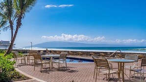 Un área al lado de la piscina con sillas de descanso y mesas, con vista al océano.