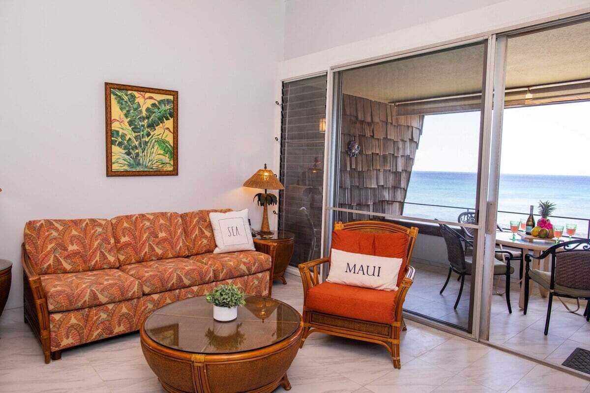 Un salon avec un canapé, un fauteuil et une table sur laquelle est posée une plante. Une fenêtre offre une vue sur la mer.
