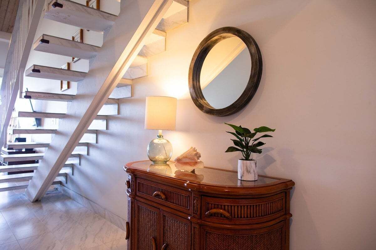 Un escalier avec des rampes blanches, un meuble en bois avec un miroir, une lampe et une plante en pot.