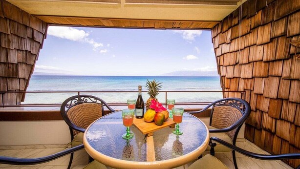 Una mesa redonda con sillas, una botella, piña y vasos en un balcón con vistas al mar.