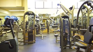 Ein Fitnessstudio mit verschiedenen Trainingsgeräten, einer Spiegelwand und Hanteln im Hintergrund.