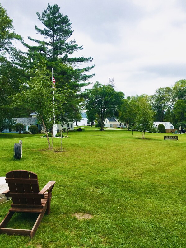 A grassy yard with a flagpole, a wooden chair, and a bench.