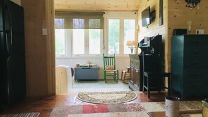 A cozy living room with a wooden ceiling, a blue sofa, a green chair, a fireplace, and a television on the wall.