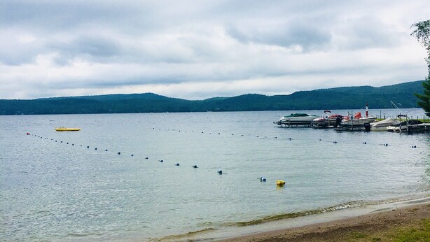 A lakeside view with a dock, calm water, and distant hills.