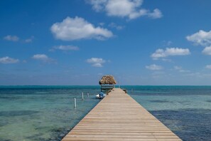 A wooden pier extending into clear turquoise waters, leading to a thatched-roof structure. - Sunset Beach Resort "B2" - Beachfront, Free Kayaks, Bikes & More! 🏖 (San Pedro Town)
