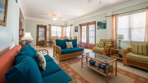 Uma sala de estar ampla com sofás azul-turquesa, móveis de vime e um ventilador de teto.