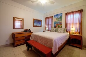 A bedroom with a bed, a wooden dresser, a bench, a ceiling fan, and a painting on the wall. - Sunset Beach Resort "B2" - Beachfront, Free Kayaks, Bikes & More! 🏖 (San Pedro Town)