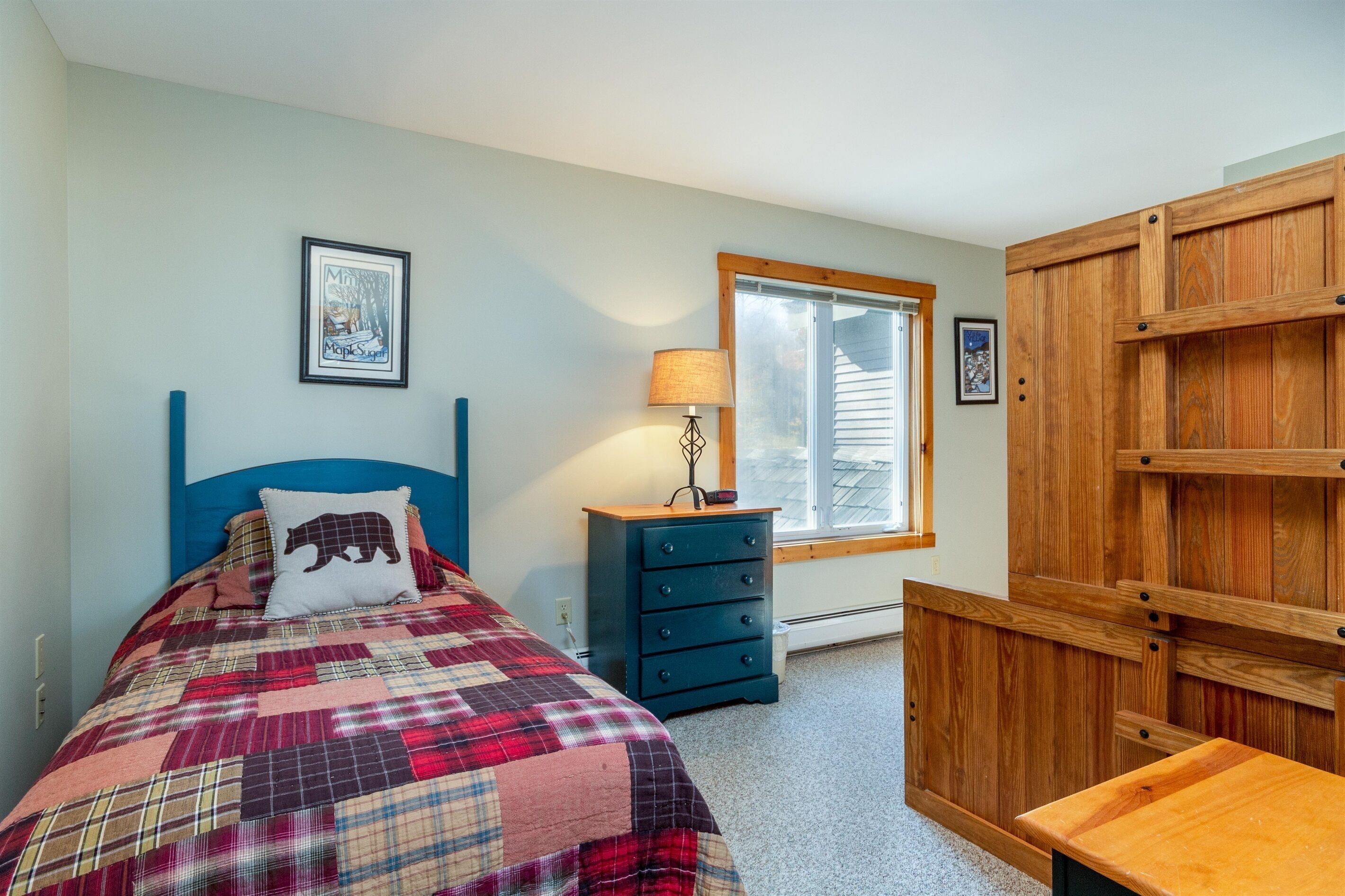 Une chambre à coucher avec un lit, une commode, une lampe et une fenêtre.