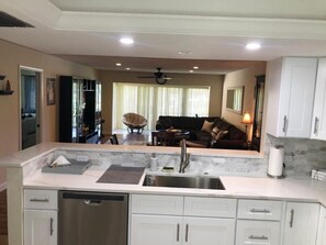 Una cocina moderna con armarios blancos, un lavamanos de acero inoxidable y un rincón comedor con sofá y mesa.