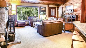 A cozy cabin interior with a stone fireplace, a large leather sofa, and a dining area with a wooden table and chairs. - Uinta Lodge by Cottonwood Lodging (Brighton)
