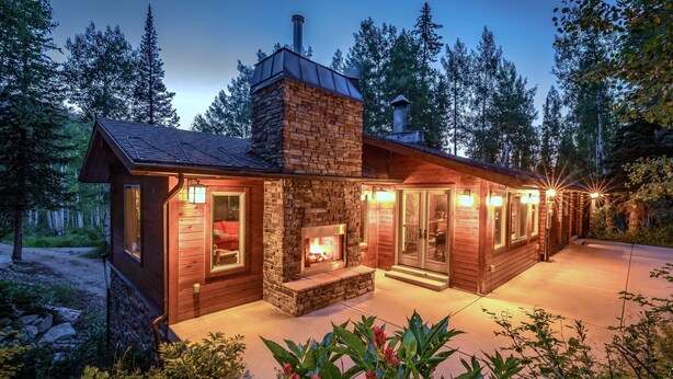 A cozy cabin with a stone fireplace, wooden exterior, and a deck area. - Uinta Lodge by Cottonwood Lodging (Brighton)