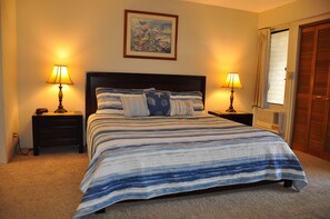 A bedroom with a bed, two bedside tables with lamps, a nightstand, a window with curtains, and a door.