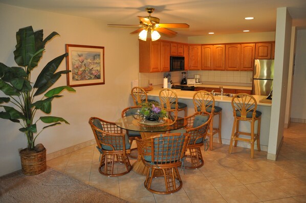 A kitchen with wooden cabinets, a stainless steel refrigerator, and a dining area with wicker chairs and a glass table.