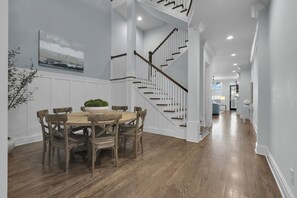 A dining area with a wooden table and chairs, a potted plant, and a staircase leading to an upper level.