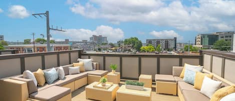 A rooftop terrace with wicker furniture, a view of the city, and a clear sky.