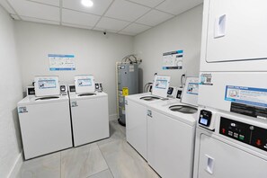 Uma lavanderia com várias máquinas de lavar e secar, cada uma com etiquetas de instruções e códigos QR.