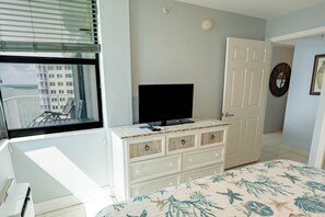 A bedroom with a bed, a dresser, a television, and a window with blinds.