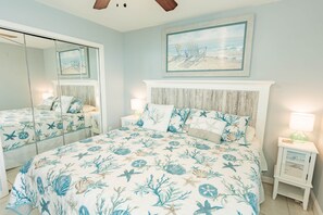 A bedroom with a large bed, a mirror, a nightstand, and a painting of a beach scene.