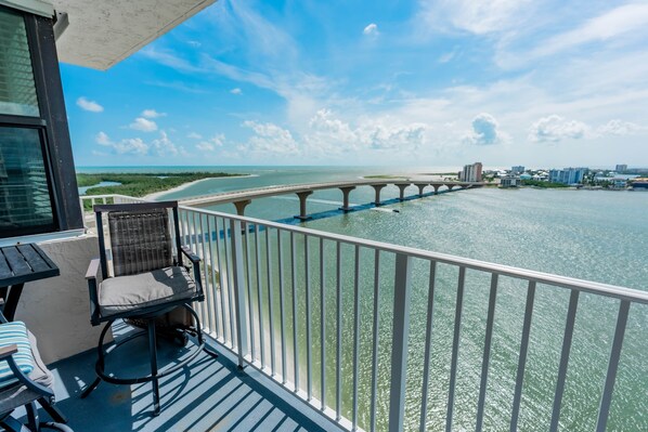 A balcony with a view of a bridge over water, a chair, and a table.