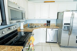 A modern kitchen with white cabinets, a stainless steel refrigerator, a built-in oven, a microwave, and a coffee maker.