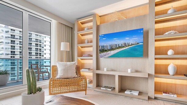 Una sala de estar moderna con un ventanal grande, una silla de mimbre, un televisor de pantalla plana y estanterías de madera empotradas.