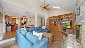 A spacious living room with a sectional sofa, a fireplace, a bookshelf, and a television. - WALK to Beach, Town of Dewey w/LARGE Heated POOL thru Oct, HOT TUB and fire pit! (Dewey Beach)