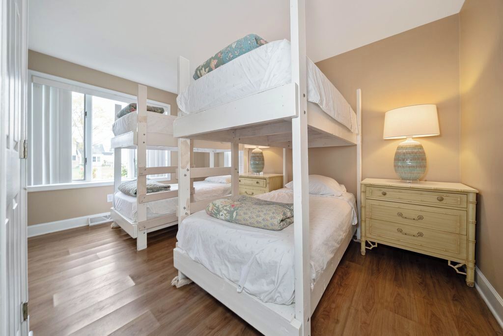 Quarto com beliche, janela, luminária de cabeceira e cômoda.