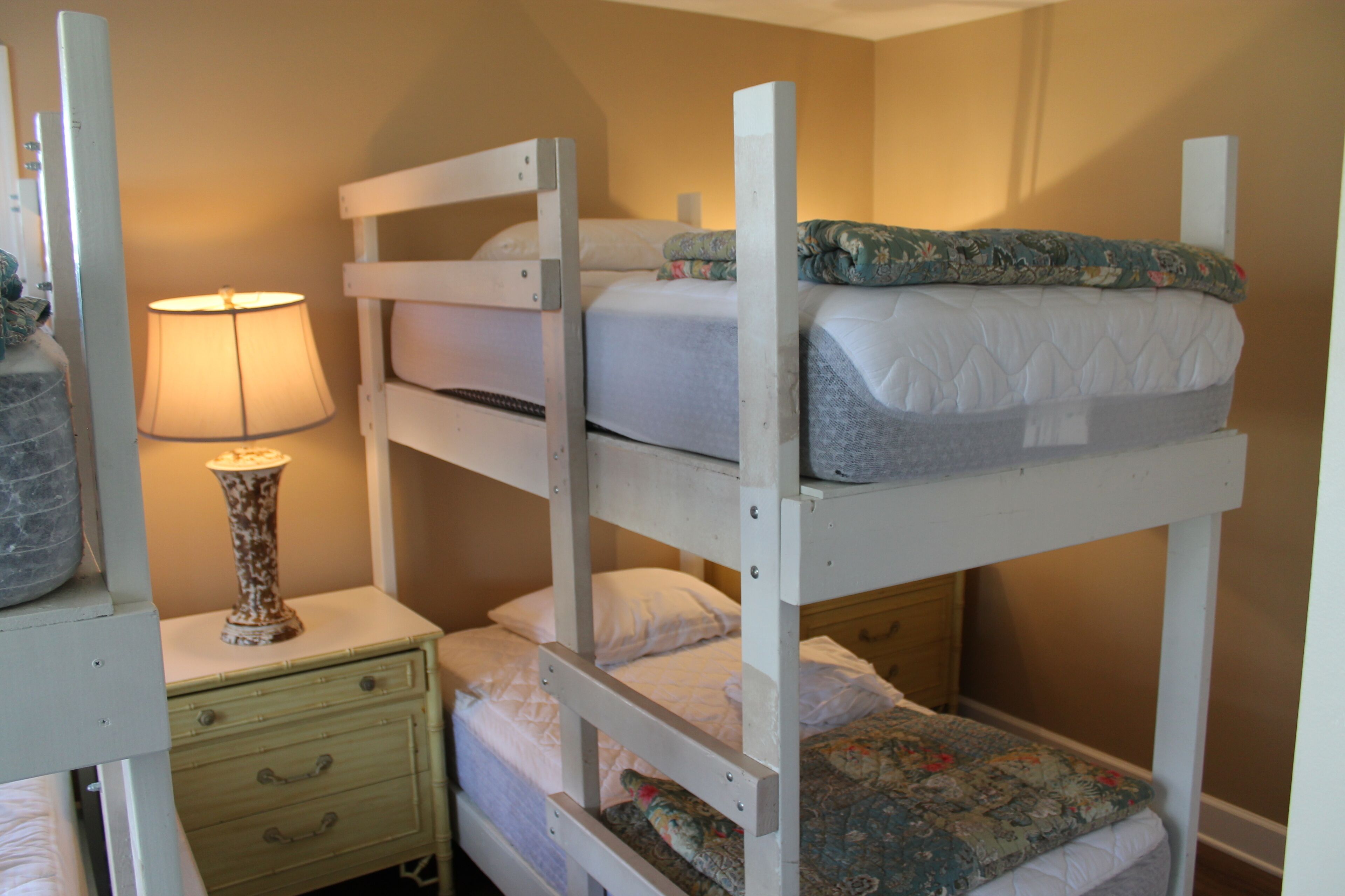 A bunk bed room with a nightstand, a lamp, and a small drawer.