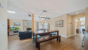 A spacious living area with a wooden dining table, blue chairs, a bench, a fireplace, and a television. - WALK to Beach, Town of Dewey w/LARGE Heated POOL thru Oct, HOT TUB and fire pit! (Dewey Beach)