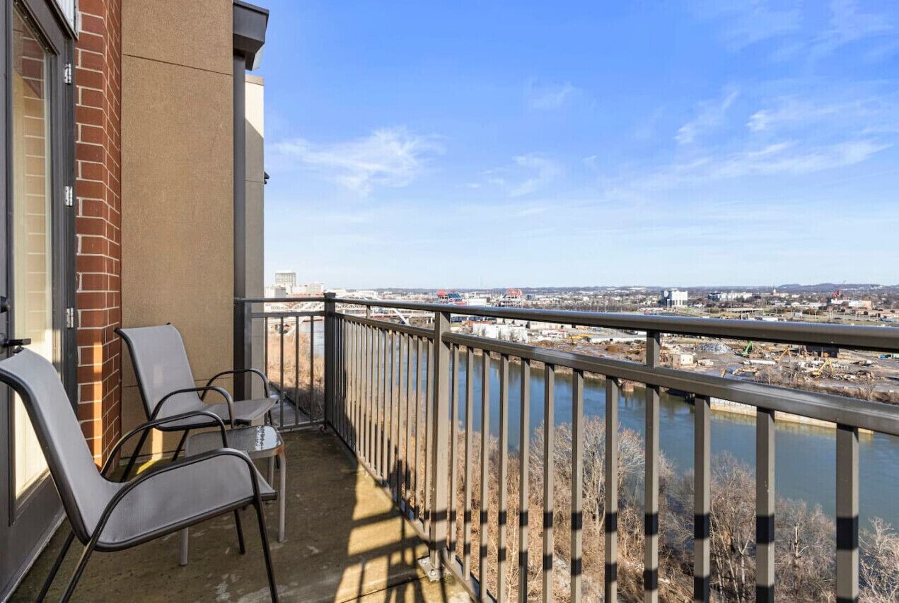 A balcony with two chairs and a table, overlooking a river and cityscape.