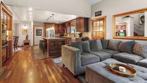 Ein geräumiges Wohnzimmer mit einem grauen Modulsofa, Holzböden und einer Küche im Hintergrund.