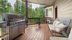 Eine überdachte Terrasse im Freien mit einem Weber-Grill, einer gepolsterten Sitzbank und Blick auf einen Wald.
