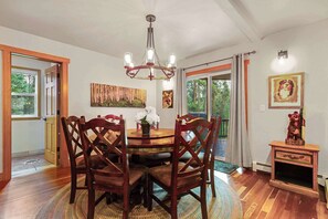Uma sala de jantar com mesa e cadeiras de madeira, um candelabro e uma lareira.