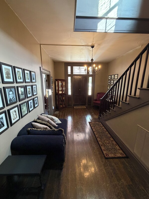 Un salón espacioso con un sofá azul oscuro, piso de madera y una escalera que sube a otro nivel.