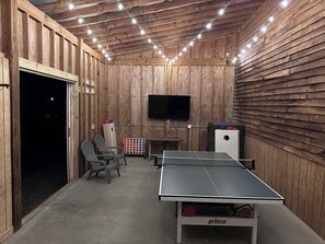 A wooden room with a ping pong table, chairs, a TV, and string lights. -  Historic Lexington Retreat - 5BR on Acres- Perfect for Families, Friends & Pets (Lexington)