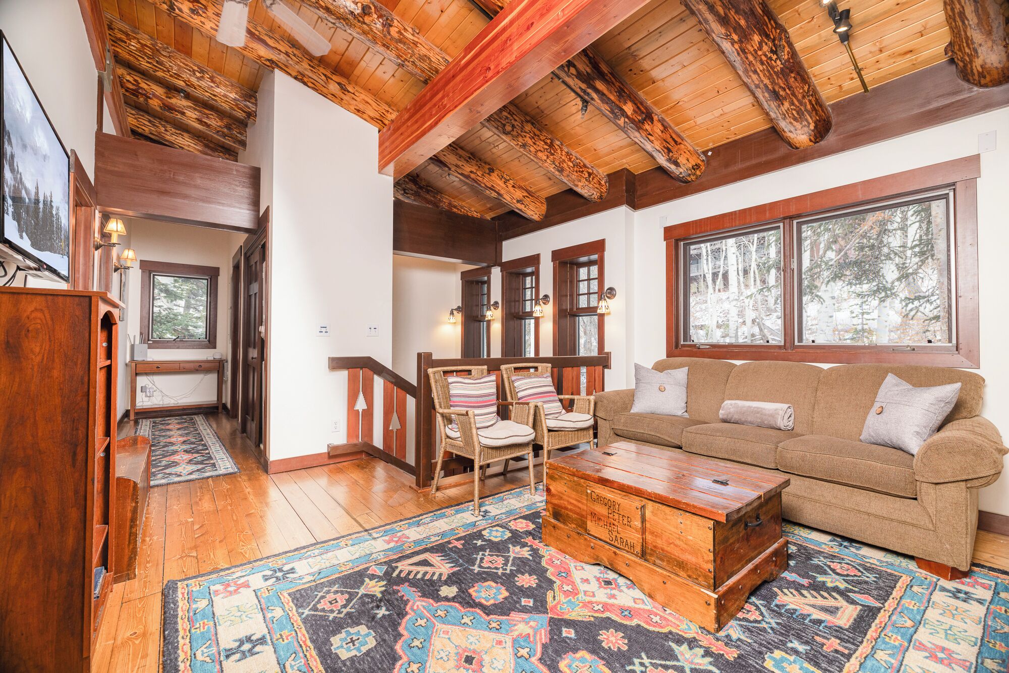 A cozy living room with a wooden ceiling, a brown sofa, a coffee table, and a patterned rug.