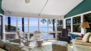 Une pièce lumineuse, baignée de soleil, avec vue sur la mer, comprenant un canapé, deux fauteuils, une table et une lampe.