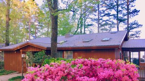 Une cabane en bois surmontée d’un toit en métal, entourée d’une végétation luxuriante et de fleurs roses éclatantes.
