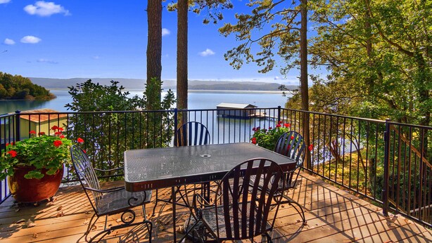Une terrasse avec une table et des chaises donnant sur un lac, entourée d’arbres et agrémentée d’une rambarde.