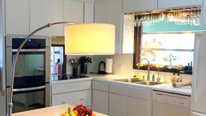 Une cuisine moderne avec des meubles blancs, un four encastré, un lave-vaisselle et un panier à fruits posé sur le plan de travail.