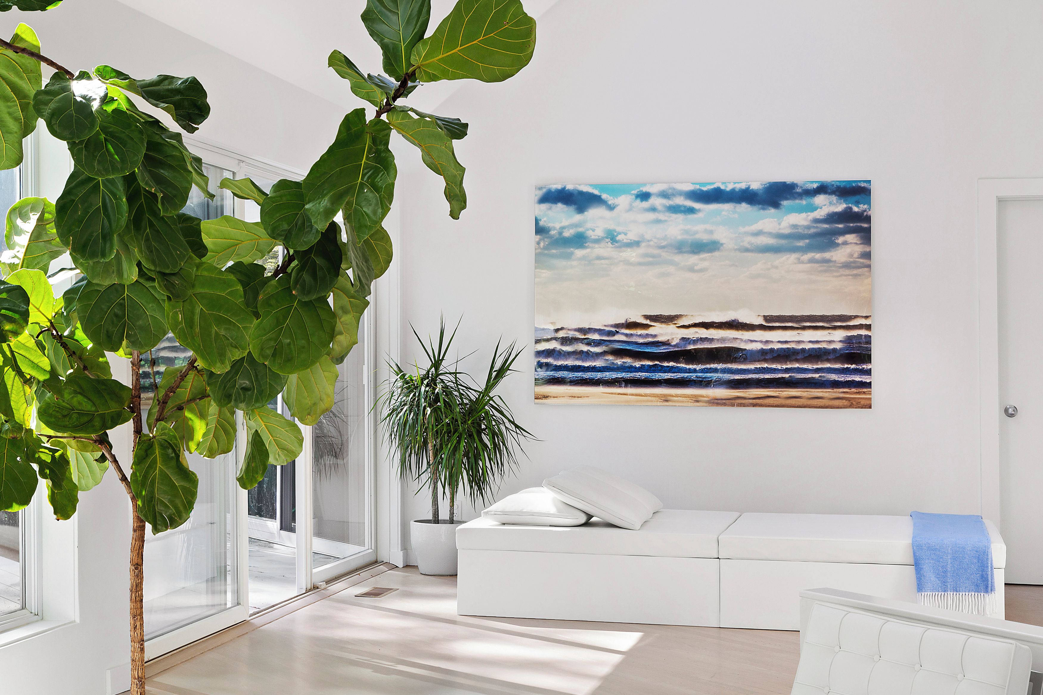 A modern living room with a large window, a white sofa, and a beach painting on the wall.