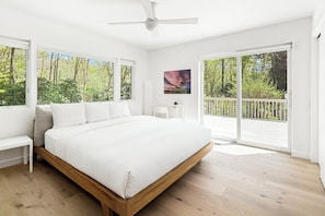 A bedroom with a large bed, a ceiling fan, a view of the outdoors through a sliding door, and a painting on the wall.