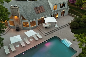 A two-story house with a swimming pool, outdoor furniture, and a deck.
